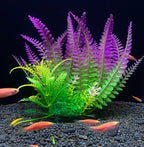 Artificial aquarium plants with green and purple leaves on a dark gravel background